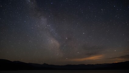 Fototapeta premium This image is a realistic photograph of a starry night sky over a dark landscape. The sky is a deep indigo to dark grey, heavily populated with countless stars.