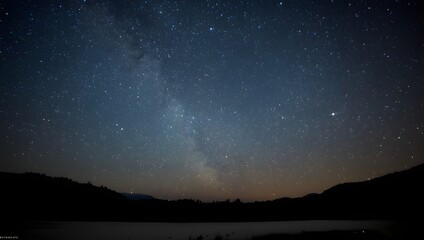 Fototapeta premium This image is a realistic photograph of a starry night sky over a dark landscape. The sky is a deep indigo to dark grey, heavily populated with countless stars.