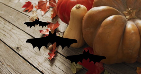 Pumpkins and autumn leaves with flying bats image over wooden background