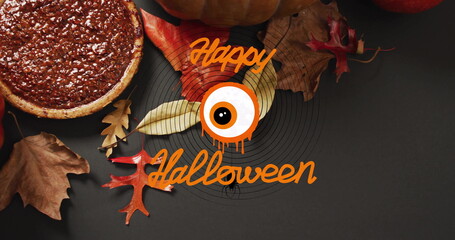 Happy Halloween text with eyeball image over autumn leaves and pumpkin pie