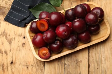 Ripe cherry plums, green leaves and cloth on wooden table, flat lay