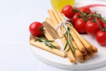 Delicious grissini sticks, rosemary and fresh tomatoes on white table, closeup. Space for text
