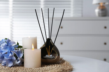 Spa composition of holder with incense sticks, burning candles and flowers on white table indoors,...