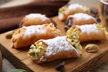 Delicious cannoli with ricotta cheese, peanuts, pistachios, chocolate and powdered sugar on wooden table, closeup