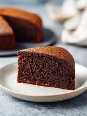 Deliciously Moist Chocolate Cake Slice Served on a Light Plate With Blurred Background of Whole Cake