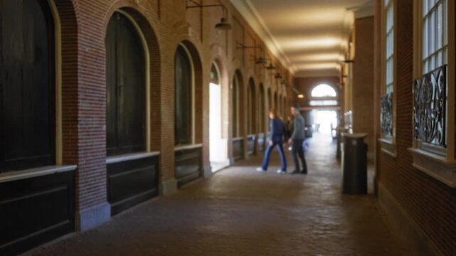 Blurry corridor in a historic university building with defocused figures walking along the bokeh-lit pathway showcasing the old brick architecture.