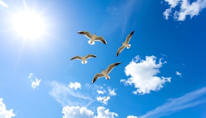 Obraz premium Four seagulls soar gracefully through a vibrant blue sky, dotted with fluffy white clouds, highlighting a sunny day.