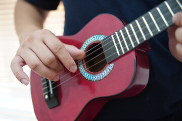 Asian man playing ukulele at home