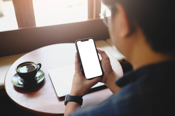 Over the shoulder view of a man holding a smartphone with a blank white screen, sitting in a cafe...