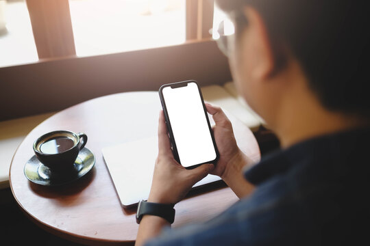 Over the shoulder view of a man holding a smartphone with a blank white screen, sitting in a cafe with coffee. Ideal for app or website mockups. - Powered by Adobe