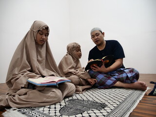 Asian muslim father teaching his daughter how to read recite Quran