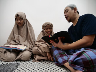 Asian muslim father teaching his daughter how to read recite Quran
