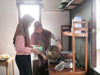 Indonesian muslim woman preparing meals in kitchen with her daughter, cooking traditional authentic asian food