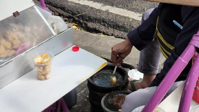 Indonesian Street Vendor Skillfully Prepares Spicy Tahu Gejrot Sauce in a Traditional Stone Mortar