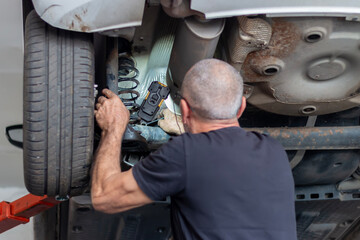 A mechanic senior man checking the brake, tyre, undercarriage of car in workshop at auto car repair...