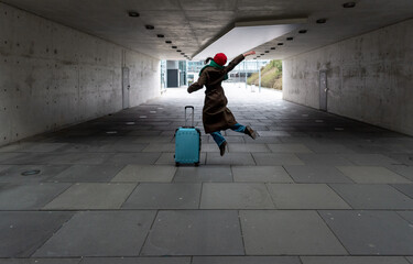 Woman traveler carrying a trolley and jumping of joy near Stuttgart airport