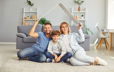Happy young family father, mother and son sitting on floor in living room and looking at camera...