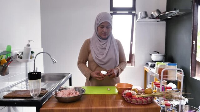 Asian muslim woman peeling, cutting and slicing onion and garlic. Preparing marinade for chicken meat