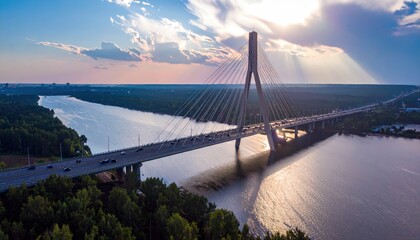 Obraz premium Aerial view of a cable-stayed bridge over a river at sunset with dramatic clouds and sunbeams