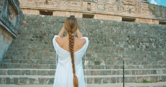 Woman filming ancient stepped structure of Mayan ruins during Mexico tour