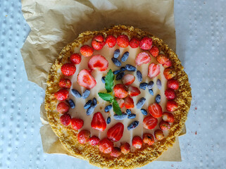  beautifully decorated homemade fruit tart with fresh wild strawberries blueberries and mint sprig...