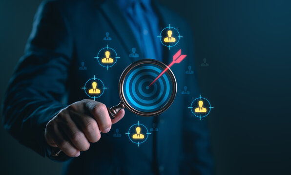 Businessman holding magnifying glass targeting specific audience or customer group, representing marketing strategy, customer segmentation, lead generation, recruitment process and business focus.