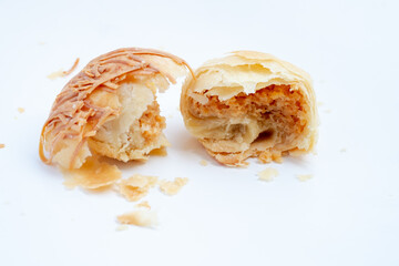 A golden-flaky pia pastry, torn in half to reveal the savory filling and texture inside. The close-up shot on a white background captures the rustic details of this traditional Indonesian snack.