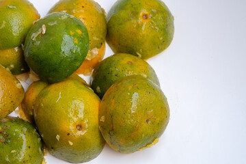 Partially squeezed calamansi limes with exposed pulp and glossy peel, showcasing the vibrant green-orange tones of fresh Indonesian citrus on a clean surface.