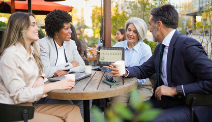 Diverse business team analyzing marketing data on digital tablet during a coffee break at outdoor cafe