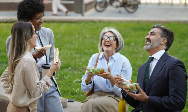 Multiethnic business team enjoying healthy lunch outdoors, laughing and talking together