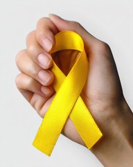 Fototapeta na wymiar Close up of a hand gently holding a yellow ribbon, symbolizing support for suicide prevention and childhood cancer awareness