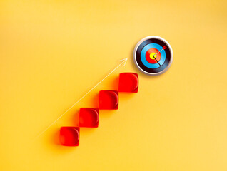 Red blocks forming upward stairs leading to 3d target with arrow hit bullseye on yellow background....