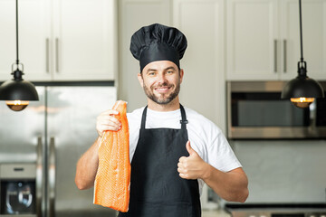 Chef with raw meat fish salmon fillet on kitchen. Chef man in uniform on kitchen. Handsome man chef...
