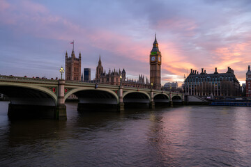 Obraz premium Westminster at Dawn: Iconic London landmarks, the Palace of Westminster and Big Ben, are beautifully silhouetted against the soft hues of dawn, reflecting on the calm water of the river Thames.