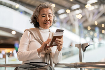 Senior asian woman holding passport and smartphone at airport showing digital travel, trip preparation and modern lifestyle for older travelers, travel app flight check-in, ticket booking, retirement
