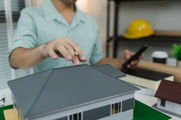 Asian male architect working with a calculator at his desk in a modern office. Surrounded by house...