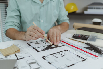 An architect uses a metal triangle ruler to draw precise lines on house blueprints laid out on a...