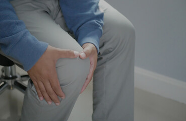 Businessman sitting on a chair for a long time causing knee pain. Young man's hands around her...