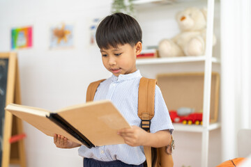 Asian schoolboy reading book with backpack in class learning new things with confidence, back to...
