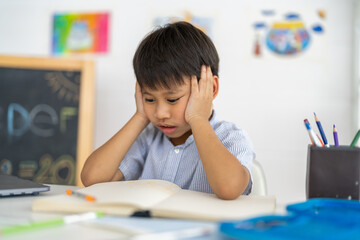 Asian boy stressed homework studying with hands on head, tired expression shows school pressure...