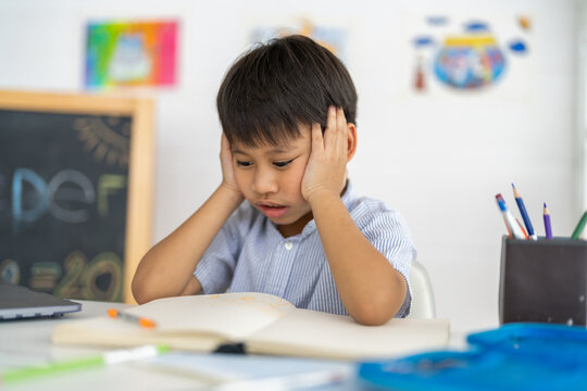 Asian boy stressed homework studying with hands on head, tired expression shows school pressure from parents, education overload with books, online learning, academic pressure and homework frustration - Powered by Adobe