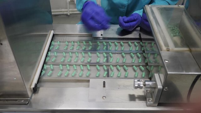 Production of medicines under human control. Pill machine dropping pills into blister packaging pockets. A pharmaceutical line worker checks the tablets and loads them into containers.