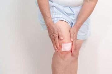 Elderly woman having knee ache with Medicated pain relief patch plaster to Runners Knee or Patellofemoral Pain Syndrome, osteoarthritis, arthritis, rheumatism and Patellar Tendinitis. Senior health