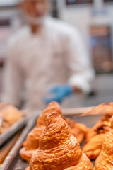 Freshly baked croissants in a bakery with a baker in the background