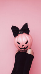 Pink halloween pumpkin head with black bow and black dress on woman against pink background, playful and spooky festive mood