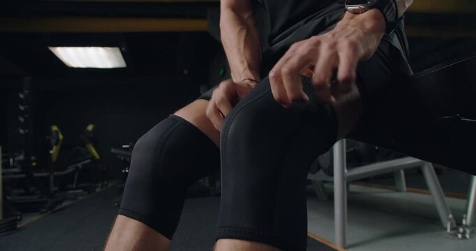 Close-up of a male athlete adjusting his knee brace in a gym, focusing on fitness and injury prevention. Athlete Adjusting Knee Brace Preparing for Workout in Gym