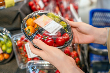 Person holding a plastic container of fresh mixed tomatoes in a supermarket