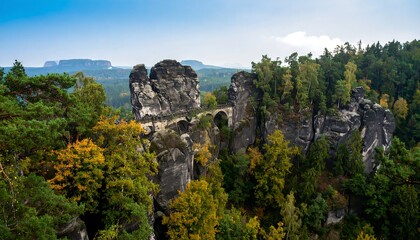 Naklejka premium Majestic sandstone formations with a winding bridge, a scenic view of autumn foliage and lush forest.