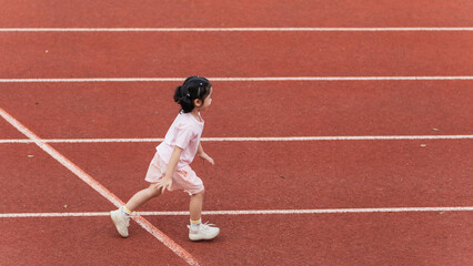 Fototapeta premium Young child in pink outfit running on a red track, showcasing determination and joy in athletic activity, capturing the essence of childhood play and movement