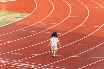 Fototapeta premium A Young Girl Walks Alone on a Red Outdoor Track While Leaving Footprints Behind, Symbolizing Journey and Exploration in Childhood